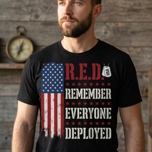 Peut inclure: T-shirt noir avec un drapeau américain vieilli et le texte "R.E.D. Remember Everyone Deployed." Comprend un graphique de plaque d'identité américaine. Le t-shirt est à col rond.