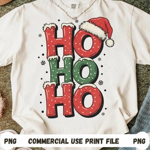 Peut inclure: T-shirt blanc avec un motif festif "Ho Ho Ho" en rouge et vert, orné de flocons de neige et d'un bonnet de Père Noël. Le design a un aspect vintage et vieilli, idéal pour les fêtes.