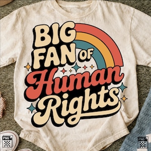 May include: A cream-colored t-shirt featuring a graphic design with the text BIG FAN OF Human Rights in bold, retro-style lettering. The design includes a multi-colored rainbow arch in orange, yellow, and teal, accented by small four-pointed stars.