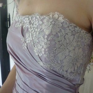 K&ouml;nnte beinhalten: Ein tr&auml;gerloses Kleid mit einem Lavendel-Satin-Oberteil und einer wei&szlig;en Spitzen-&Uuml;berlagerung. Das Oberteil ist gerafft und die Spitze ist zart und filigran.
