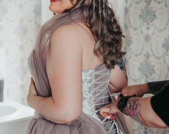 Abito da sposa in tulle grigio tortora e pizzo avorio. Chiusura a corsetto sul retro, sopragonna removibile e spalline.