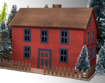 May include: A red papercraft house with a brown roof and black windows. The house is surrounded by small green pine trees and a brown picket fence.