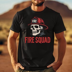 May include: Black t-shirt featuring a skull wearing a firefighter's helmet with the word "FIRE" on it. The words "FIRE SQUAD" are printed in red below the skull graphic. The shirt is made of a soft material.