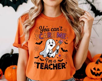 May include: Orange t-shirt with the text "You can't SCARE ME I'm a TEACHER" and a cartoon ghost holding a pencil. The shirt has a Halloween theme with bats and spiderwebs.