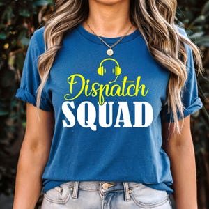 Puede incluir: Una camiseta azul con las palabras "Dispatch SQUAD" en amarillo y blanco. La palabra "Dispatch" está en una fuente cursiva, y la palabra "SQUAD" está en negrita. Encima de la palabra "Dispatch" hay un gráfico amarillo de auriculares.
