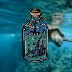 May include: Embroidered patch featuring a bottle with a cork top. Inside, a tropical island scene with a palm tree, sun, and whales swimming in the ocean. The patch has a teal and blue color scheme with a black border.