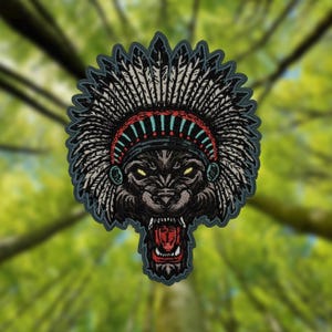 May include: Embroidered patch featuring a wolf's head wearing a Native American headdress. The patch has a black, gray, red, and blue color scheme. The wolf's mouth is open, revealing its teeth. The background is a blurred image of a forest.