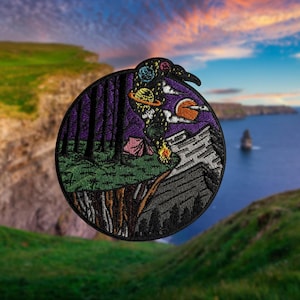 Puede incluir: Parche bordado que representa una escena de bosque oscuro con una tienda de campaña, un acantilado y un cielo estrellado con planetas. El parche es circular y tiene un fondo negro.