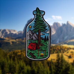 May include: A blue glass bottle with a cork top, containing a miniature scene of a campsite in a forest. The scene includes a red tent, a green tree, a small stream, and a campfire.
