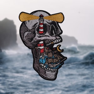 May include: An embroidered patch depicting a skull with a lighthouse in its eye and a ship in its mouth. The lighthouse is red and white striped with a yellow beam. The ship is blue and white with a crescent moon on the mast.