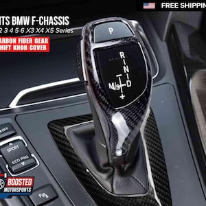 May include: Carbon fiber gear shift knob cover for BMW F-Chassis 1, 2, 3, 4, 5, 6, X3, X4, and X5 series. The cover features a black and gray carbon fiber weave pattern. The gear shift knob has the letters P, R, N, D, and M/S+.