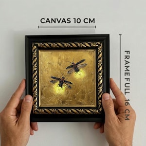 May include: A square painting of two fireflies on a gold background, encased in a black and gold ornate frame. Text indicates a canvas size of 10 cm and a full frame size of 16 cm. The fireflies feature glowing yellow abdomens and dark wings.