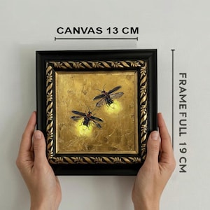 May include: A square painting of two fireflies with glowing yellow abdomens on a textured gold background, encased in a black and gold ornate frame. The canvas measures 13 cm, and the full frame measures 19 cm as indicated by the text labels.