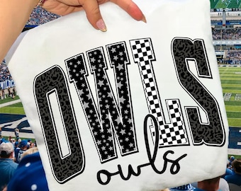 May include: White t-shirt featuring the word "OWLS" in a bold, stylized design. The letters have a mix of patterns, including leopard print, stars, and a checkered pattern. The word "owls" is written in cursive below the main text.