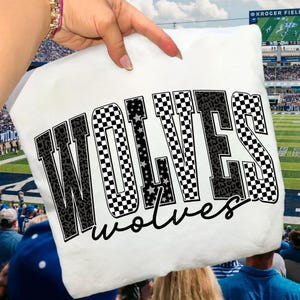 May include: White pillow with the word "WOLVES" in large, bold letters. The letters have a mix of checkered, leopard print, and star patterns. The word "wolves" is written in a cursive font below the main word.