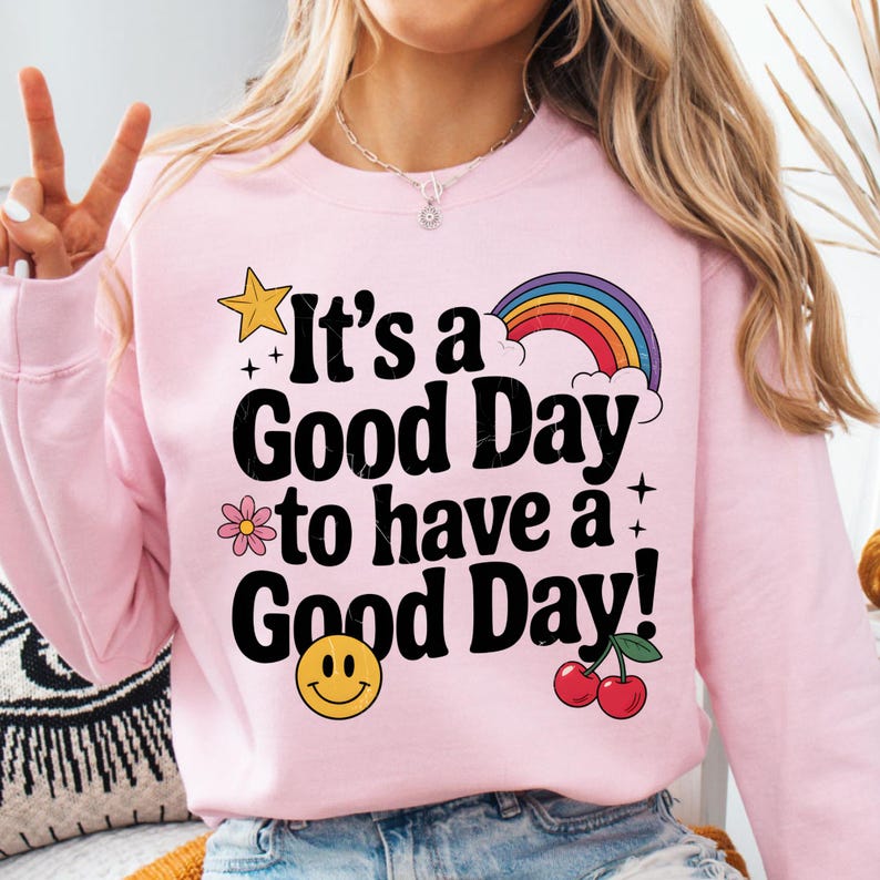 K&ouml;nnte beinhalten: Rosafarbener Pullover mit einem Regenbogen, einem Stern, einer Blume, einem Smiley und Kirschen. Der Text auf dem Pullover lautet "It's a Good Day to have a Good Day!"