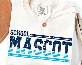 May include: An off-white crew neck t-shirt with a Comfort Colors label at the collar. The front features the text SCHOOL MASCOT in a distressed navy blue and light blue font, with horizontal lines integrated into the design of the letters.