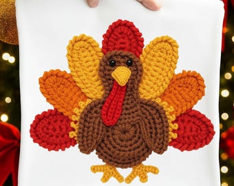 May include: A white square pillow featuring a crocheted turkey design. The turkey has a brown body, red wattle, yellow beak, and colorful feathers in shades of red, orange, and yellow. The pillow is held by a person.