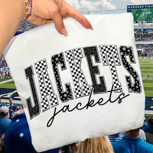 May include: White cushion featuring the word "JACKETS" in large, bold letters, with checkered, leopard print, and star patterns. The word "jackets" is written in a cursive font below. A football stadium is visible in the background.
