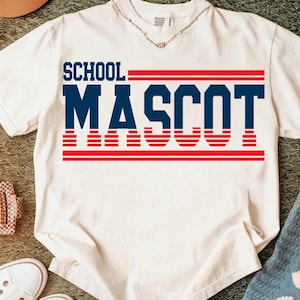 May include: A white t-shirt with the words "SCHOOL MASCOT" printed in navy blue and red. The text is arranged in a bold, blocky font, with the word "MASCOT" prominently displayed. The shirt is made of a soft material.