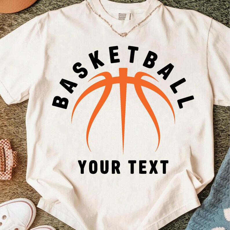 Peut inclure: T-shirt blanc avec un motif de basket-ball orange et noir. Le mot "BASKETBALL" est arqu&eacute; au-dessus du graphique, avec le texte "YOUR TEXT" en dessous. Style d&eacute;contract&eacute;.