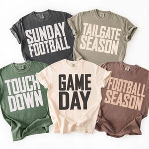 May include: Five short-sleeved t-shirts in various colors, each with a bold, white graphic. The shirts display the phrases "Sunday Football," "Tailgate Season," "Touch Down," "Game Day," and "Football Season." The shirts are casual wear.
