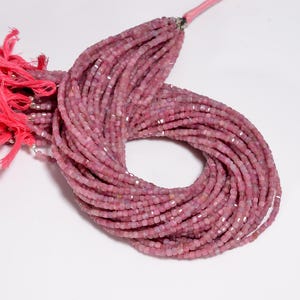 May include: A necklace of pink gemstone beads. The beads are small, square-cut, and have a slightly translucent appearance. A pink tassel is attached to the end of the necklace. The beads are strung together.