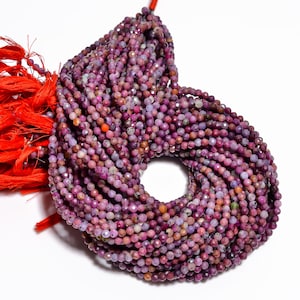 May include: A bundle of small, faceted beads in shades of purple, pink, and gray. The beads are strung together, forming a circular shape. A red tassel is visible on the left side of the image.