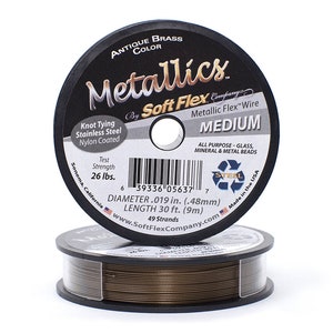 Op de afbeelding: Een spoel met Soft Flex Metallic Flex draad in antieke messingkleur. De spoel is gelabeld met "Metallics" en "Soft Flex Company". De draad is 9 meter lang en heeft een diameter van 0,48 mm. De draad is gemaakt in de VS en is geschikt voor alle soorten glas-, mineraal- en metalen kralen.