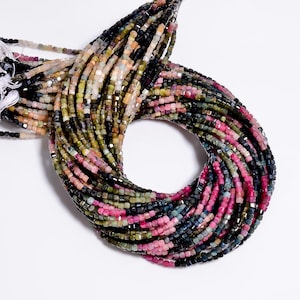 May include: A multi-strand necklace composed of small, faceted, square-shaped beads in a variety of colors including black, pink, green, and blue. The beads are strung on thin white thread, creating a dense, circular arrangement of gemstone beads.