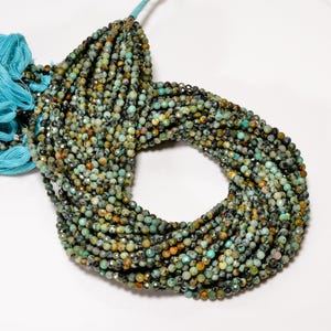 May include: A strand of small, faceted round beads in shades of turquoise, teal, brown, and black, featuring a natural mottled pattern. The beads are strung together and finished with a bright cyan blue tassel at the top of the strand.