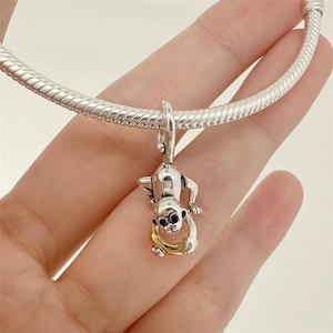 Puede incluir: Charm de plata con un mono colgado boca abajo, sosteniendo un plátano dorado. El charm de mono está unido a una pulsera de plata. El mono tiene ojos negros y está detallado con metal plateado.