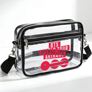 May include: A transparent crossbody bag with black edging and a black shoulder strap. The bag displays the text "BTS WORLD TOUR ARIKANG" in red and white lettering.