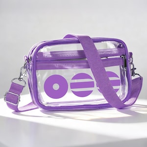 May include: A clear, purple crossbody bag with an adjustable strap. The bag has a purple zip and a design of purple circles and stripes. It features silver-coloured metal hardware.