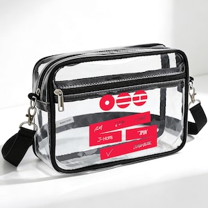 Puede incluir: Bolso bandolera rectangular transparente con ribete negro y correa de hombro negra ajustable. El bolso tiene cierre de cremallera negro y etiquetas rectangulares rojas con texto blanco. Hay un cierre plateado.