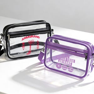 May include: Two transparent crossbody bags with black and purple trim. One bag has black straps and red text reading "ARMYRANG". The other has purple straps and white text: "WORLD TOUR ARIRANG".