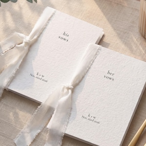 Può includere: Due libretti per voti nuziali in carta bianca testurizzata legati con un nastro di seta bianca sfilacciato. Un libretto riporta la scritta his vows, l'altro her vows, entrambi con il testo k + w e Nov. 02rd 2026 in carattere serif nero.