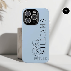 May include: A light blue phone case with the text "Mrs. WILLIAMS FUTURE" in black script. The case has a black camera module and black side buttons. The word "SKY" is in a black circle in the upper right corner.