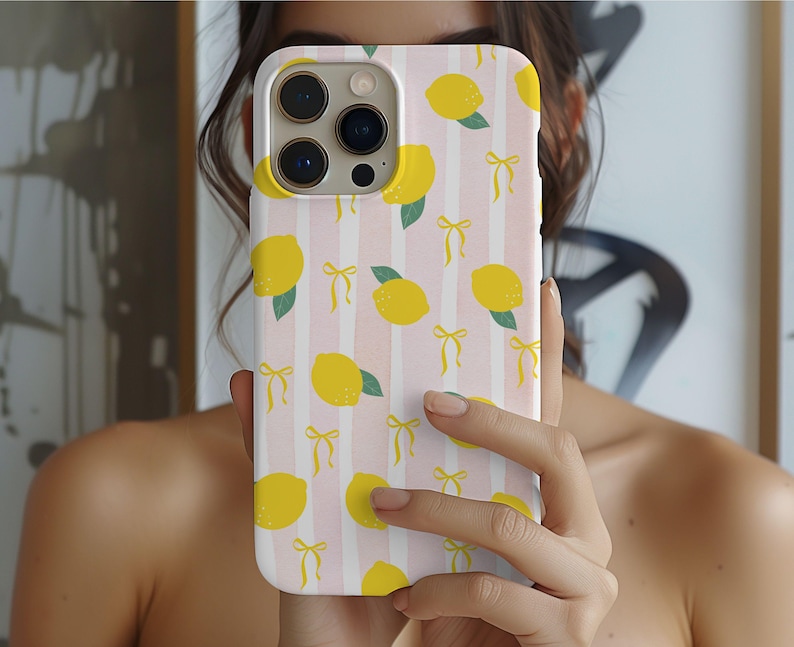 A phone case with a design featuring yellow lemons and green leaves. The lemons are interspersed with small yellow bows. The case is fitted on a smartphone with three visible camera lenses and a flash.
