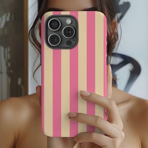 May include: A mobile phone case featuring a pink and beige striped design. The case has a camera module with three lenses and a flash.