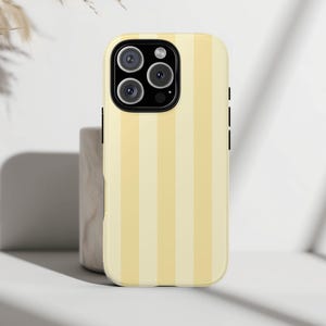 May include: A yellow and cream striped phone case. The case has a black camera module and black side buttons. The case is designed to fit a smartphone. The background is a neutral white.