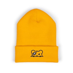 May include: Mustard yellow beanie with a black and white graphic of a bear with an eye patch. The beanie is made of a soft, knitted material and has a folded cuff. The graphic is on the front of the cuff.