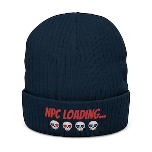 Puede incluir: Un gorro de punto azul marino con el texto bordado "NPC LOADING..." en rojo. Debajo del texto hay cuatro pequeños gráficos de calaveras, cada uno con un corazón o un ojo de diferente color: rojo, rosa, azul y blanco.