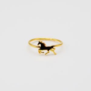 Könnte beinhalten: Ein goldener Ring mit einer Silhouette eines galoppierenden Pferdes. Der Ring ist schlicht und elegant.