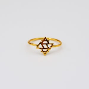 May include: A gold-colored ring with a geometric star design. The ring features a thin band and a detailed star-shaped centerpiece with open spaces. The ring is set against a white background, highlighting its metallic shine.