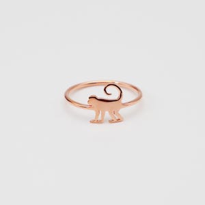 May include: A rose gold ring with a monkey silhouette design.