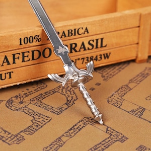 Full set display of the Zelda Link Master Sword Letter Opener with Triforce base, placed stylishly on a wooden surface for a modern collectible look. This functional miniature sword is ideal for opening letters or packages, while serving as fantasy desk decor and a gamer conversation piece. A must-have holiday gift idea for fans of Tears of the Kingdom, Breath of the Wild, and Ocarina of Time, combining nostalgia with practicality for birthdays, Christmas, and Halloween.