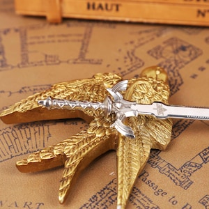 Zelda Master Sword Letter Opener displayed on a wooden desk with its Triforce base stand, showcasing the polished metal blade and detailed hilt. This image highlights the fantasy-inspired design of the letter opener, perfect as a Zelda fan collectible, Christmas gamer gift, or geek office decor piece. Ideal for fans of Tears of the Kingdom, BOTW, and Ocarina of Time, this functional mini sword adds a magical touch to any holiday gift set, Halloween display, or stocking stuffer collection.