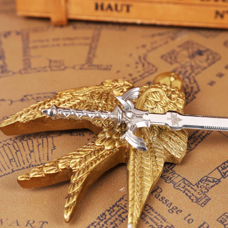 Zelda Master Sword Letter Opener displayed on a wooden desk with its Triforce base stand, showcasing the polished metal blade and detailed hilt. This image highlights the fantasy-inspired design of the letter opener, perfect as a Zelda fan collectible, Christmas gamer gift, or geek office decor piece. Ideal for fans of Tears of the Kingdom, BOTW, and Ocarina of Time, this functional mini sword adds a magical touch to any holiday gift set, Halloween display, or stocking stuffer collection.