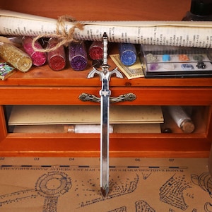 Full set display of the Zelda Link Master Sword Letter Opener with Triforce base, placed stylishly on a wooden surface for a modern collectible look. This functional miniature sword is ideal for opening letters or packages, while serving as fantasy desk decor and a gamer conversation piece. A must-have holiday gift idea for fans of Tears of the Kingdom, Breath of the Wild, and Ocarina of Time, combining nostalgia with practicality for birthdays, Christmas, and Halloween.